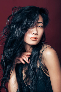 美丽的亚洲女性肖像在棕色背景。工作室长卷发的东方模特