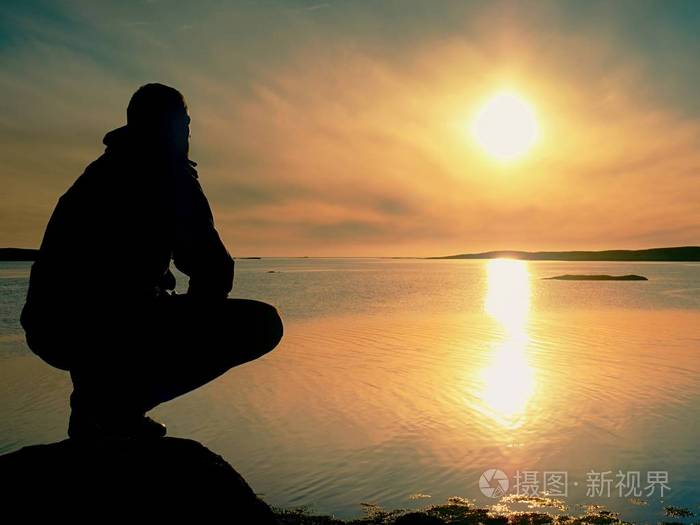 孤独的游客坐在岩石岸边思考.在美丽多彩的夕阳下放松