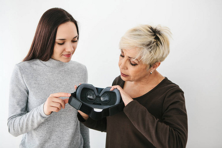 一位年轻女孩向一位老妇人解释如何使用虚拟现实眼镜。老一辈和新技术