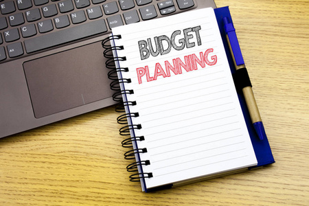 编写显示预算计划的文本。财务预算的业务概念写在笔记本上的木质背景在办公室与笔记本电脑