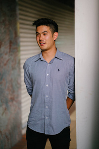 一个英俊, 年轻, 聪明的中国亚裔男子的肖像微笑着, 站在墙上的一天。他有短发, 穿着灰色西装。