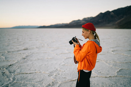 观看照片的年轻女子有野生死亡山谷土地与干燥的表面探险, 女摄影师在恶水盆地探险期间探索低地