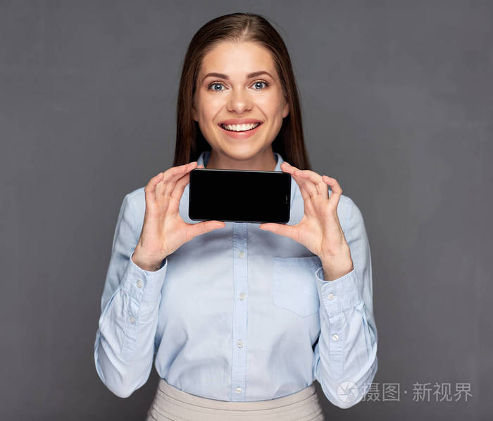 微笑的商人手持黑色智能手机在黑暗的墙壁背景微笑