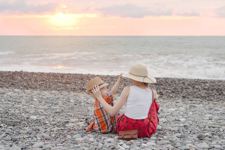 妈妈和儿子在卵石海滩玩耍。日落时间。后退视图