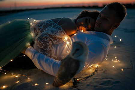新娘和新郎躺在沙漠旁边的灯泡和猫头鹰花环在日落。特写