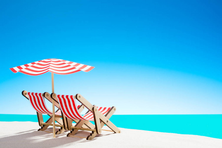 两个阳光躺椅下的沙滩上的沙滩上的海洋和天空与复制空间