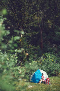 在山上露营。一个妇女坐在帐篷附近对 bac