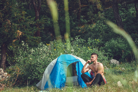 在山上露营。一个男人坐在帐篷旁边对着 backd