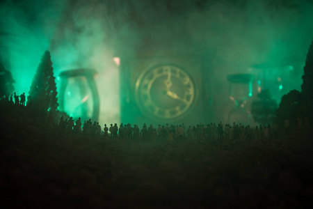 一大群人在夜间森林的剪影站立反对一个大箭头时钟与柔和的轻的光在雾背景。时间概念