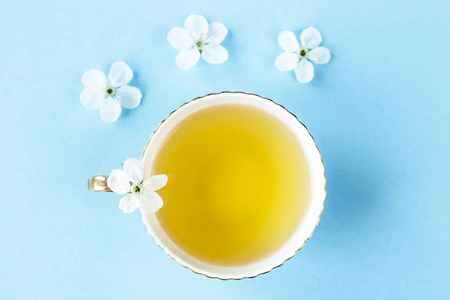 一杯蓝色精致的绿茶, 花瓣在白色的春天开花的树木的蓝色背景。春天灵感的概念。顶部视图, 平躺