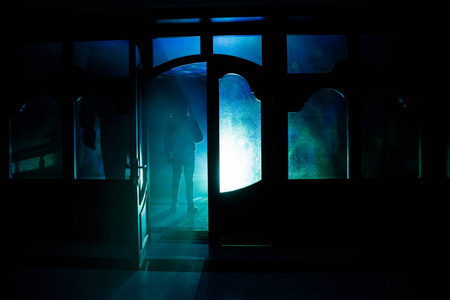 一个未知的影子身影在门通过一个封闭的玻璃门的剪影。一个人在夜晚的窗口前的剪影。恐怖场面万圣节模糊剪影概念