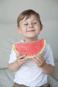 一个4岁的小可爱男孩正在吃西瓜。夏天。热。西瓜。一个带着西瓜的快乐男孩的肖像。明亮的色调。舒适