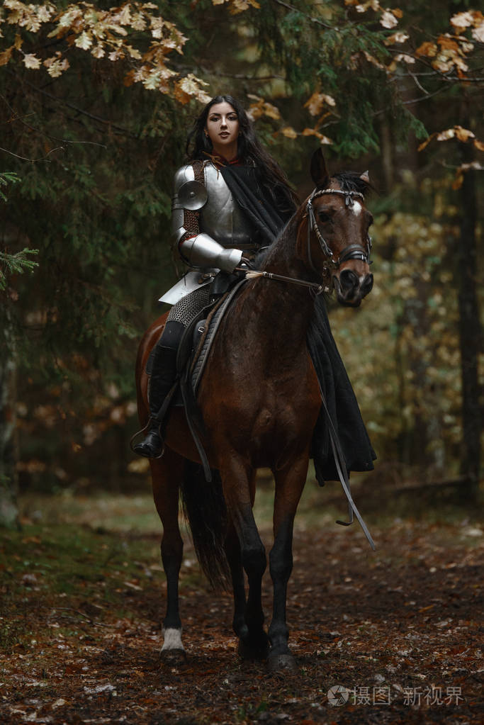 一个美丽的战士女孩用剑穿着锁链和盔甲骑在一个神秘的森林马