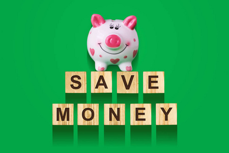字省钱, 由字母在木制建筑立方体与小猪银行。绿色背景, 孤立概念业务, 金融。背景