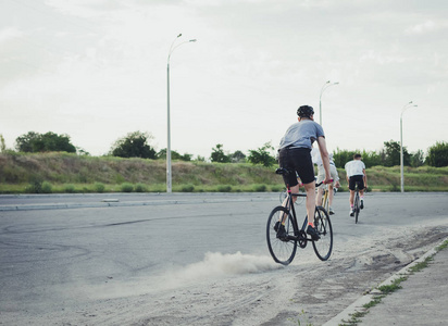 年轻的时髦男子滑动在固定的齿轮自行车在尘土的道路上