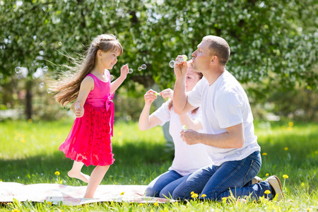 小女孩正在玩肥皂泡。父母让肥皂泡在他们的女儿在夏天在公园
