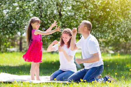 小女孩正在玩肥皂泡。父母让肥皂泡在他们的女儿在夏天在公园