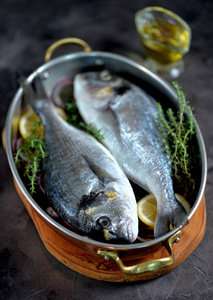 两条新鲜的鱼, 有柠檬, 红洋葱和百里香, 在铜煎锅里