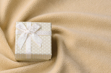 一个小的礼品盒橙色与一个小弓躺在毯子柔软和毛茸茸的橙色羊毛织物与许多浮雕褶皱。打包礼物送给你可爱的女朋友