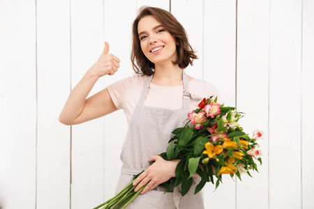 年轻漂亮的花店妇女站在花和看相机与拇指在车间