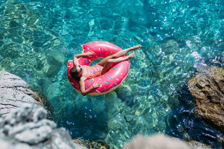 美丽的女人躺在地中海上的浮动环和享受日光浴