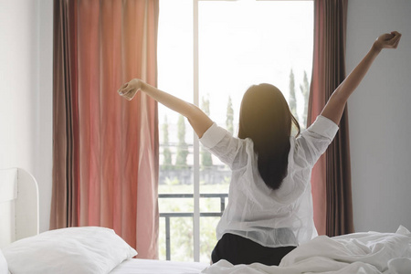 阳光照耀大地快乐的亚洲妇女在床上起床后, 早上醒来后, 在卧室阳光