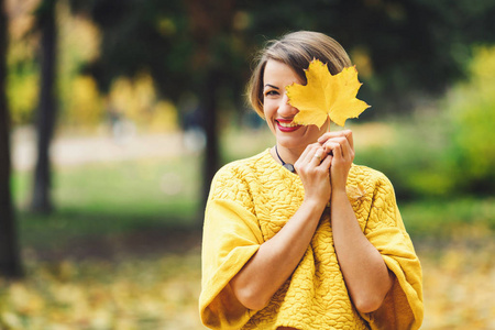 秋天公园黄色毛衣微笑的女孩关闭与枫叶的眼睛