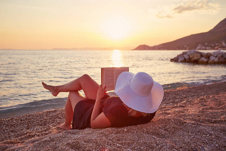 在日落的海滩上读一本书的妇女