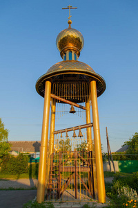 基督徒塔与木横梁铜响铃金黄十字架和圆顶在村庄清晨太阳视图从下面