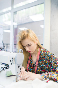 一个年轻的女裁缝正在工作在工作室的缝纫机。漂亮的女孩在一台缝纫机上工作。缝纫机上的裁缝工作