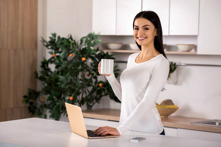 纯粹的快乐。腰部的好女人站在厨房, 而喝茶和使用笔记本电脑