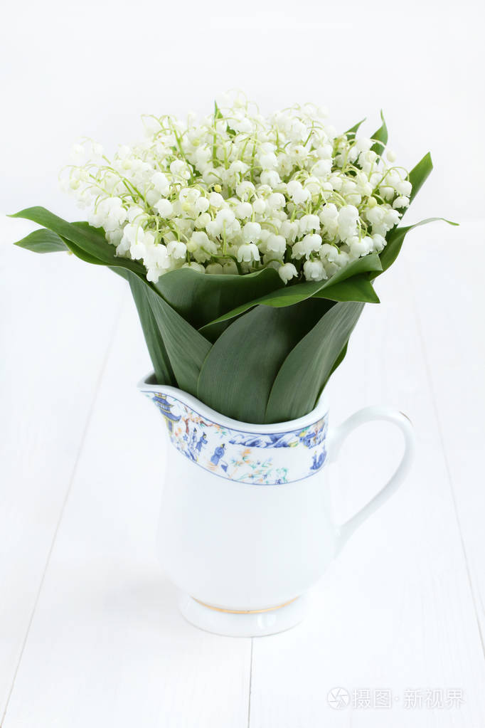 束美丽的白色漆木制的桌子上的白色水罐铃兰