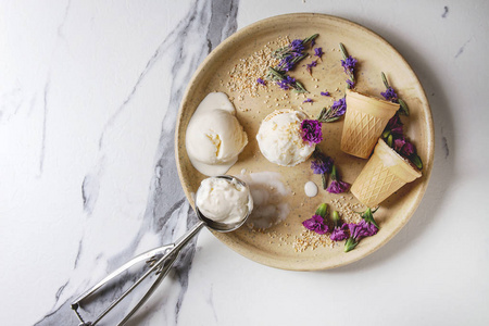 自制香草冰淇淋球与紫色的可食用花卉和金属勺在陶瓷板上的白色大理石背景。顶部视图, 空间