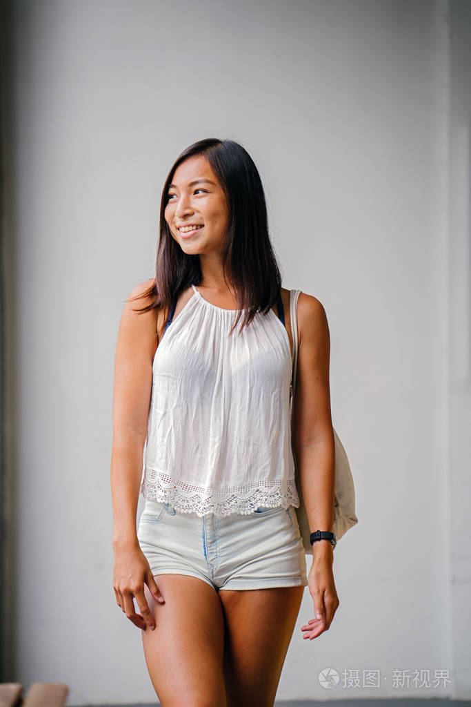 一个可爱的运动的晒黑的亚洲华人女孩的肖像在街上走着灰色的背景