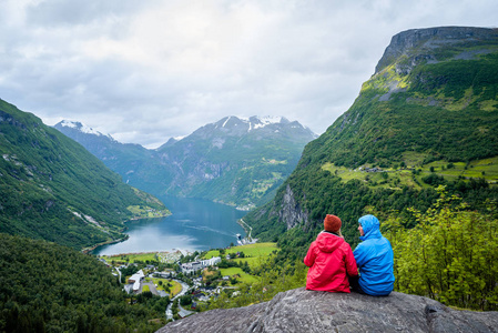 夫妇坐在岩石上, 看着海湾和山脉。挪威 Geiranger 和 Geirangerfjord 旅游村