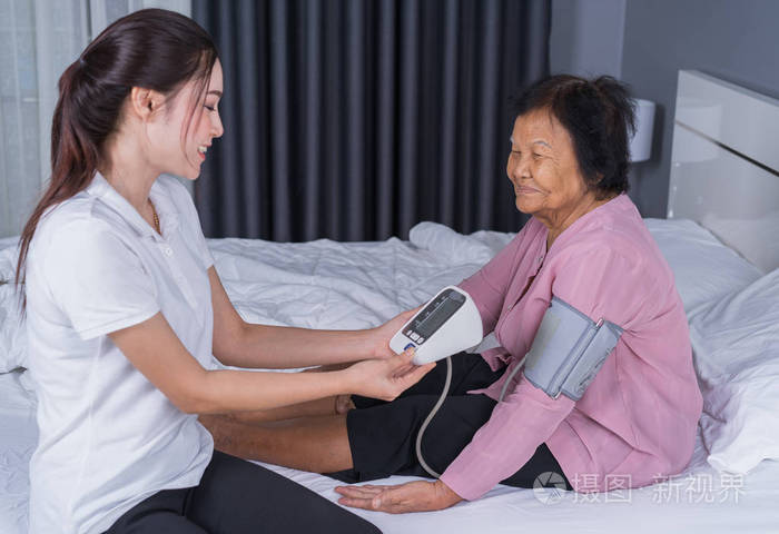 女护士在床上检查一名老年妇女的血压
