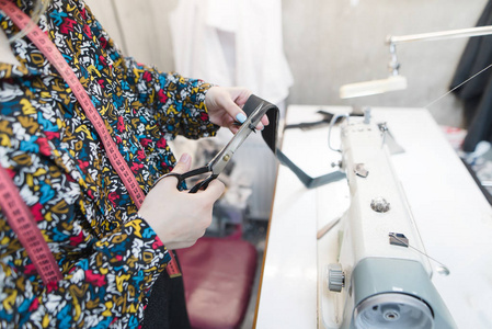 裁缝手在缝纫机和工作场所的背景下用剪刀剪布。裁缝工作在工作室裁缝衣服。职场裁缝