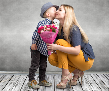 小儿子给他心爱的母亲一束美丽的玫瑰和亲吻妈妈的脸颊。春 妇女节 母亲节这一天