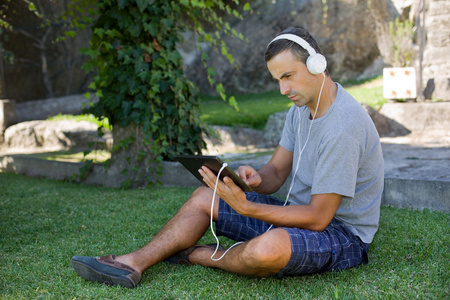 年轻人与戴着耳机的 tablet pc 听音乐放松户外公园