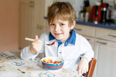 早饭吃谷物与牛奶和浆果, 新鲜草莓的小金发学校孩子男孩照片