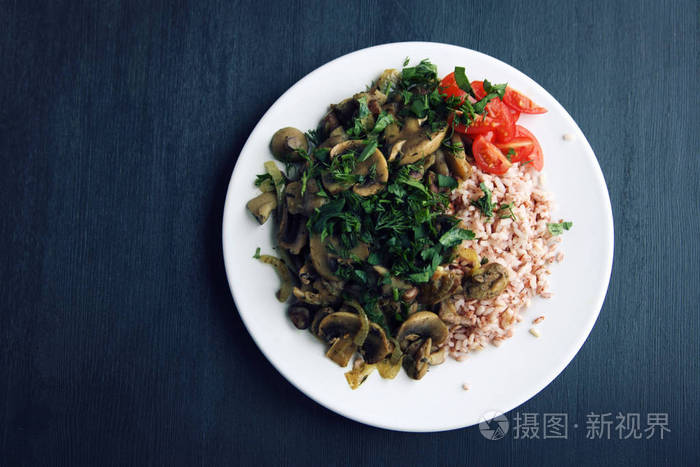 红米饭, 蘑菇和樱桃西红柿。纯素食的菜肴。欧洲菜。简单健康的午餐在黑色的背景。素米粉在白盘子上。关门了顶部视图