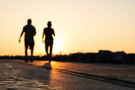 年轻夫妇赛跑者的剪影在公园在黄昏日落奔跑。人们走路和运动。健身与健康活动生活方式