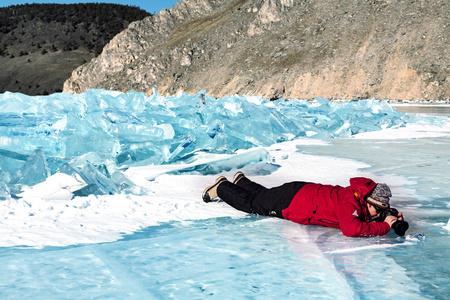 一名男子躺在冰上，用相机的红色外套