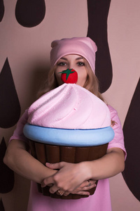 滑稽的年轻金发模特穿着粉红色的 t恤和帽子, 摆着大蛋糕甜美的装饰