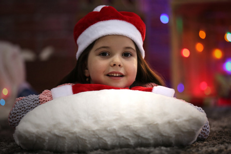 漂亮的小女孩在顶红色的帽子，躺在枕头上在圣诞节装饰的房间