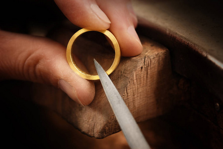 金匠手拿着一枚金戒指, 用一个金属锉, 与复制空间, 焦点, 狭窄的景深一起工作。