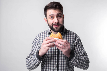 男子手持一块汉堡包。学生吃快餐。不是有帮助的食物。饿极了的家伙