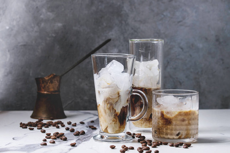 冰咖啡鸡尾酒或刨冰与冰块和奶油服务于三不同的眼镜与老式的 jezva 和咖啡豆周围的白色大理石桌子与灰色混凝土墙背景