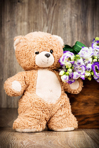 束鲜花和一只泰迪熊木制背景