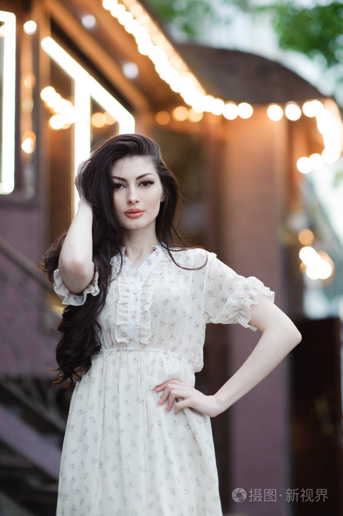 美丽的白种女孩触摸她的长发在夏季礼服背景城市咖啡馆的位置